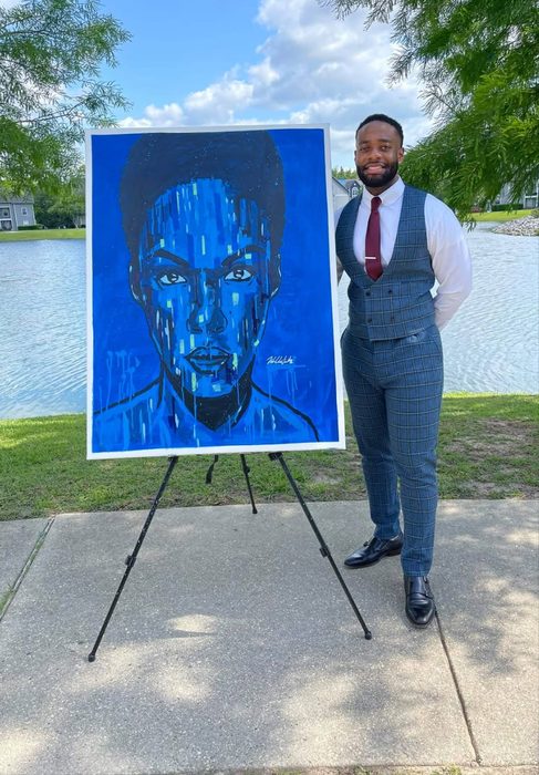 Willie Austin in a suit beside a large blue portrait on an easel by a lake