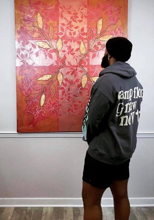 Willie Austin, seen from behind, looking at Untitled, a large red painting covered in gold leaves