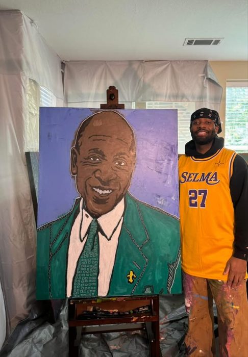 Willie Austin in a gold Selma 27 jersey beside his portrait of Coach Willie Maxey in a green jacket
